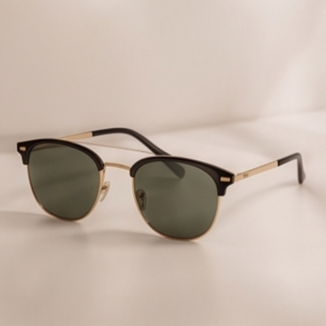 A pair of classic-style sunglasses with dark green lenses, a black acetate front, and gold metal rims and temples, resting on a light beige surface.